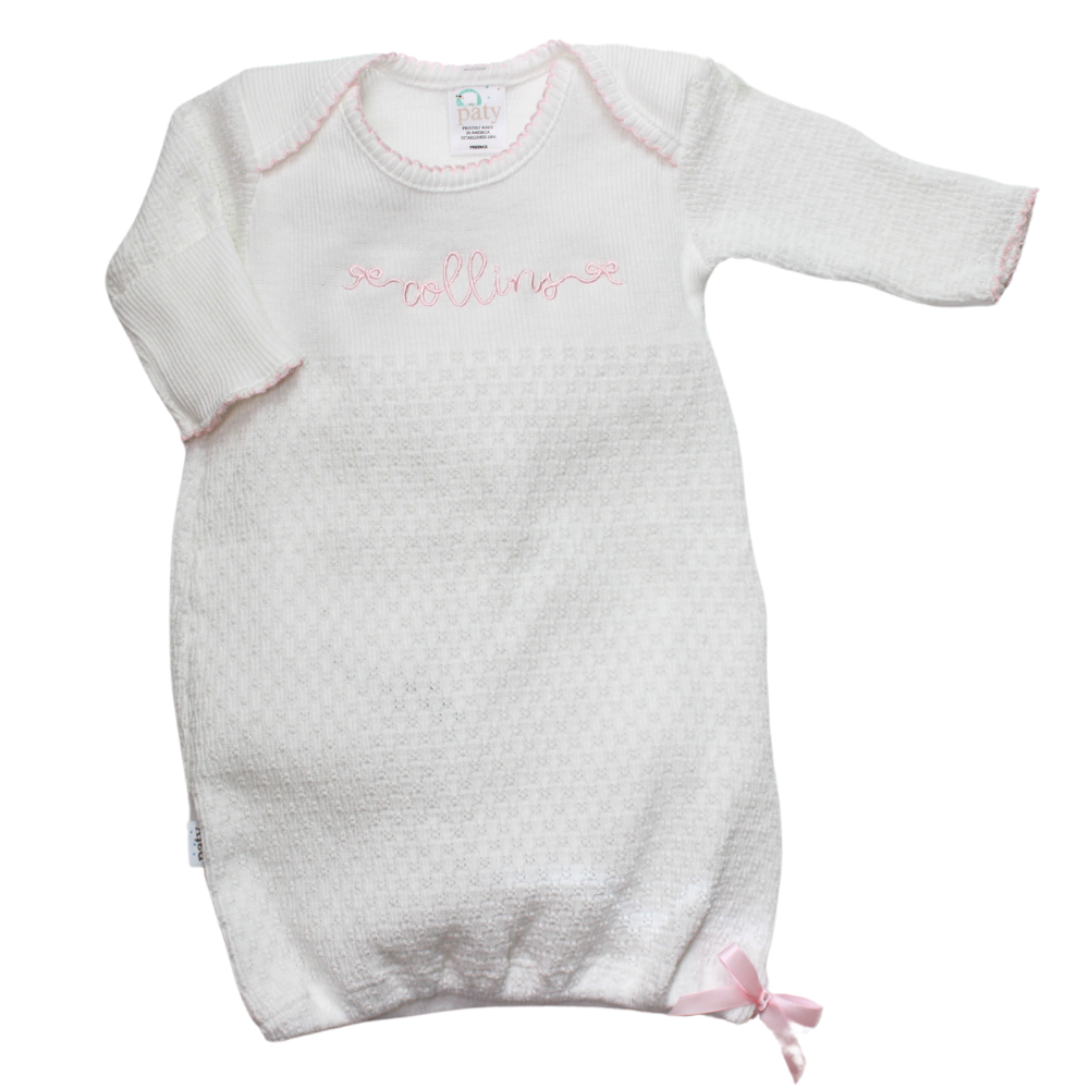 A white knit baby gown with pink trim and a pink satin bow, featuring long sleeves and a pointelle design.
